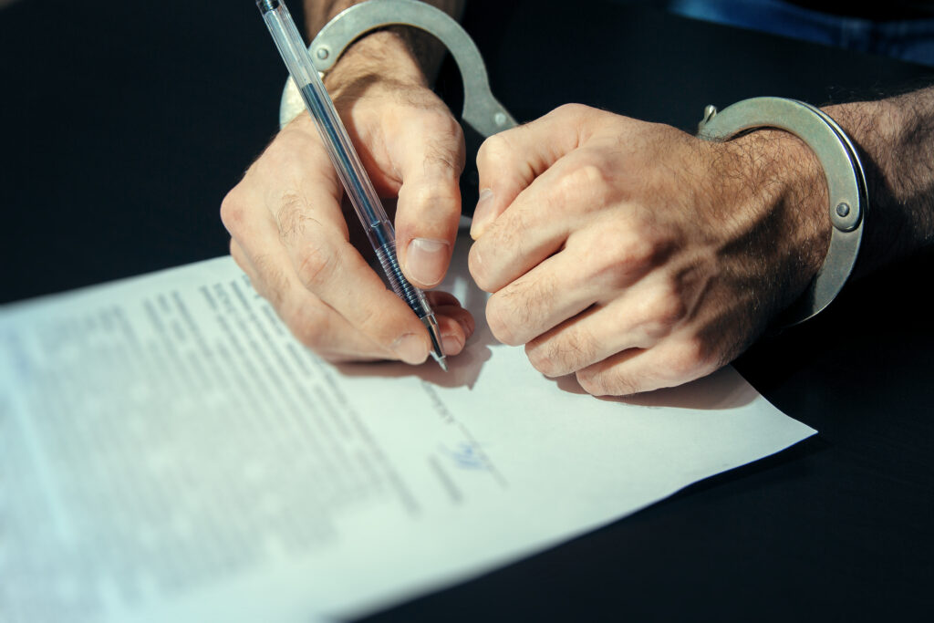 Man in handcuffs signing plea agreement